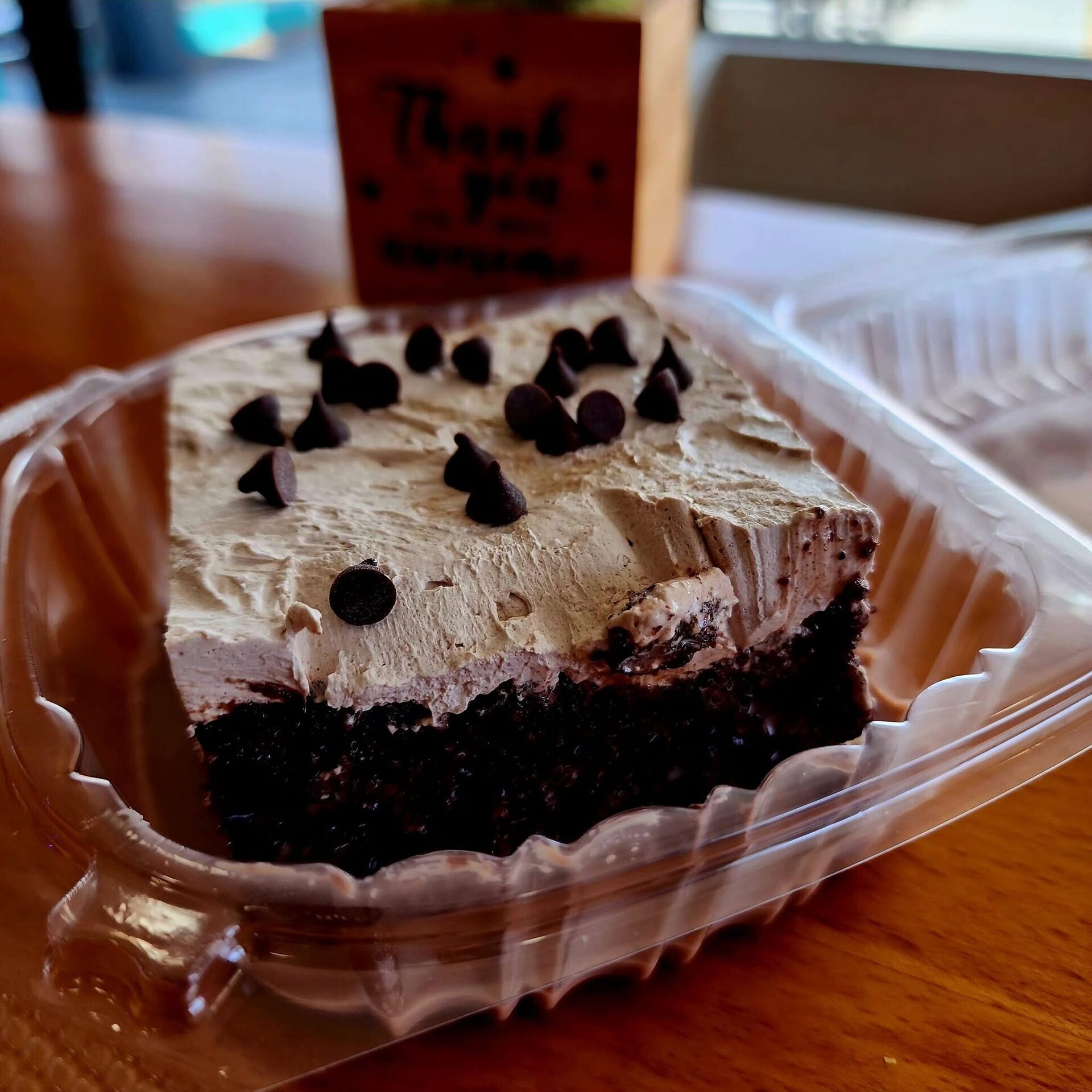 A slice of chocolate cake with chocolate chips in a to-go clamshell
